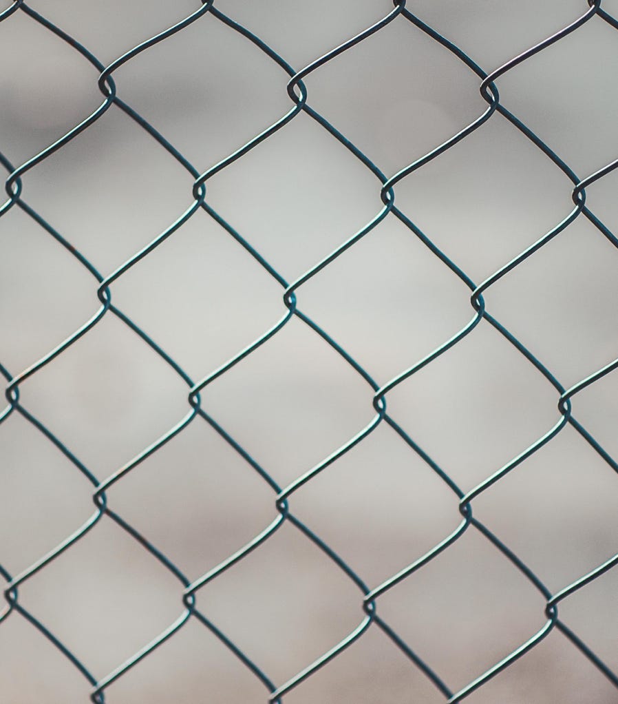 Detailed closeup of a metal chain-link fence with a blurred neutral background, perfect for textures and overlays.